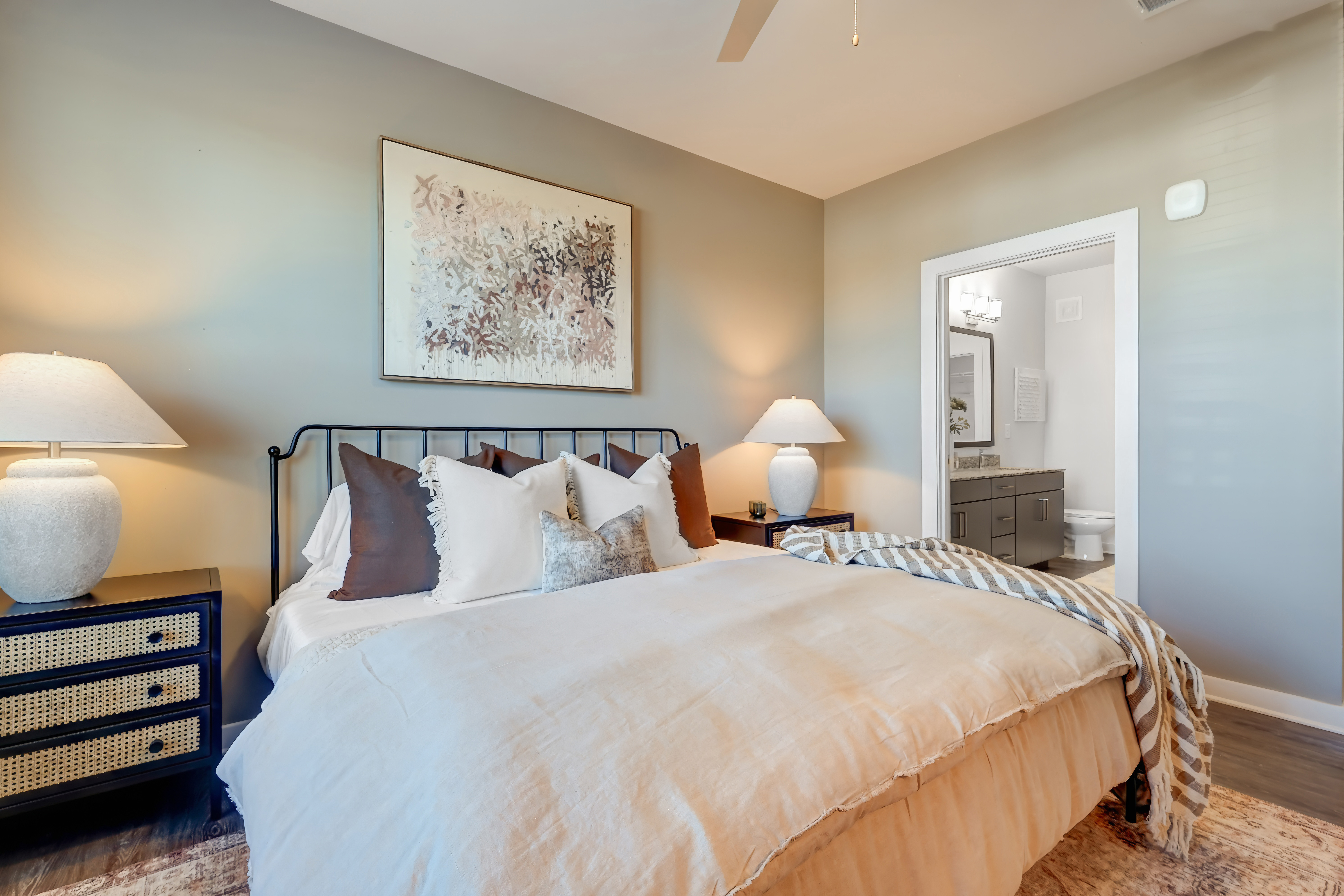Stylish bedroom with attached bathroom and designer finishes in luxury apartment home Modern bedroom with neutral tones, cozy bedding, and private ensuite bathroom in upscale apartment