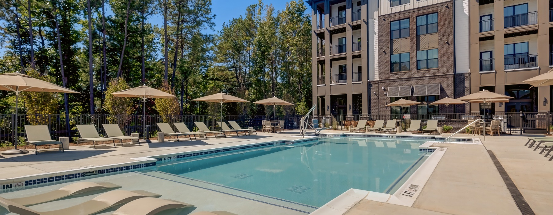 Resort-style swimming pool with sun loungers, umbrellas, and modern apartment building backdrop